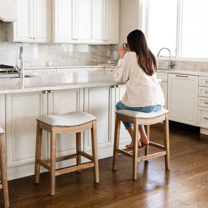 Adrien Saddle Counter Stool In Weathered Oak Finish With Sand Color Fabric Upholstery in Stools by Maven Lane